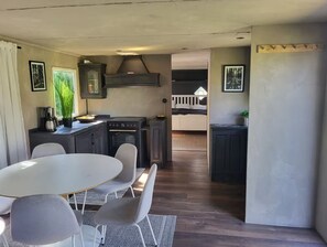 A compact kitchen with a dining area, featuring a round table and chairs, a built-in stove, and a small cabinet. - Caravan in the countryside (Gärds Köpinge)