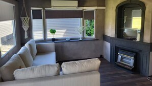 A living room with a sectional sofa, a fireplace, and large windows with blinds.