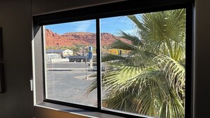 A room with a large window overlooking a parking area and a mountain. - Modern Loft w/ Red Rock Views - Downtown St George (St. George)