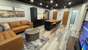 A modern living room with a sofa, a coffee table, and a kitchen area with a dining table and chairs. - Modern Loft w/ Red Rock Views - Downtown St George (St. George)