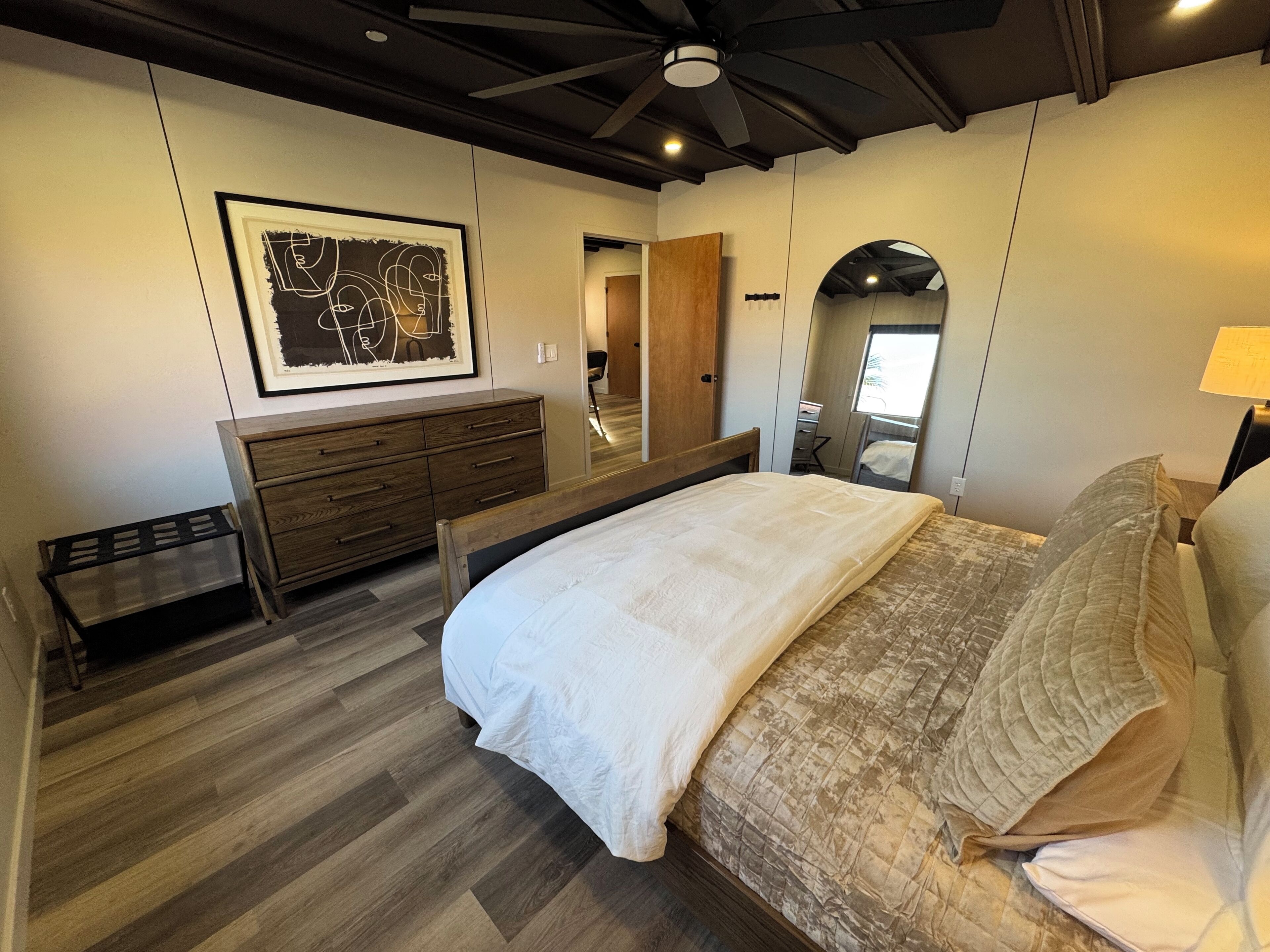 A bedroom with a bed, wooden dresser, and a large mirror.