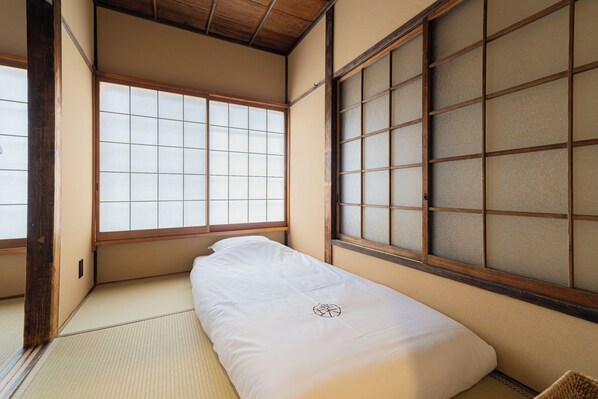 A traditional Japanese room with tatami flooring, a low bed, sliding shoji doors, and a wooden ceiling.