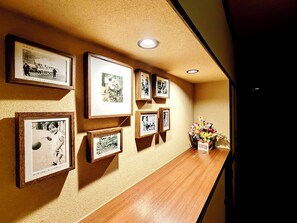 A hallway with framed photographs on the wall and a wooden shelf with a vase of flowers.