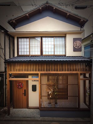 A traditional Japanese building with a tiled roof, a wooden entrance gate, and a sign with Japanese characters.