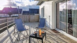 A balcony with two blue chairs, a small table with a bottle and a glass, and a view of a building with a sloped roof. - Villa Koraill Glaz by Interhome (Plouescat)