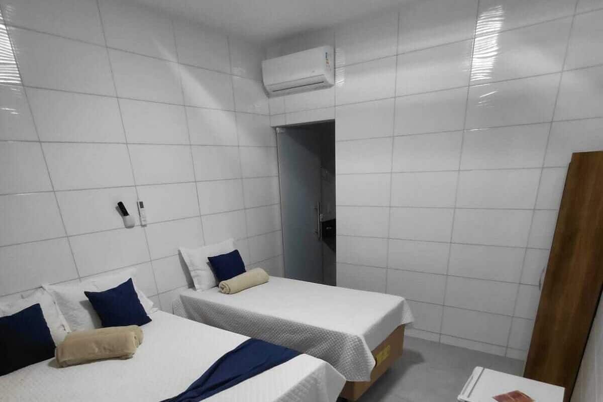 Ein Hotelzimmer mit zwei Betten, einem kleinen Nachttisch, einer Klimaanlage und einer Tür zu einem Badezimmer.