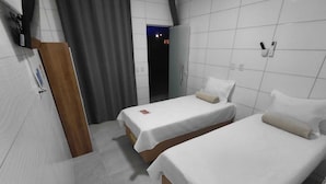 Habitación de hotel con dos camas, una puerta de madera, una cortina gris y una pared de azulejos blancos.