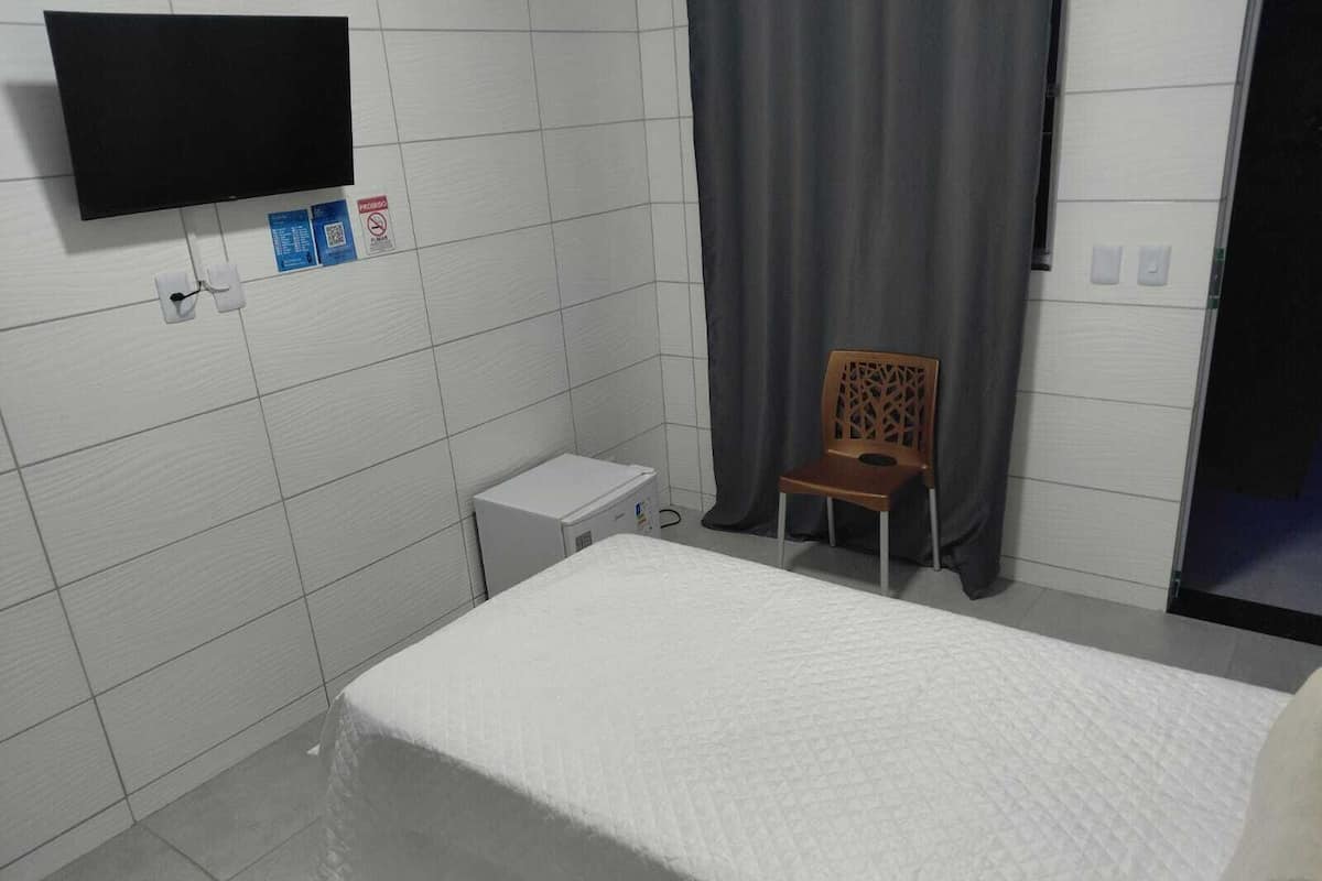 Ein kleines, sauberes Zimmer mit einem Bett, einem Sessel, einem Fernseher und einem kleinen, weißen Schrank.