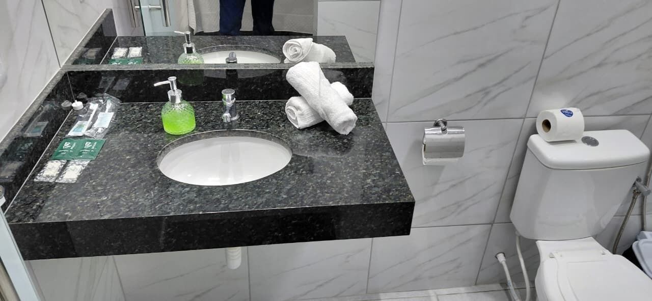 Un baño con lavamanos de mármol negro, dos espejos, un inodoro blanco y un rollo de papel higiénico.