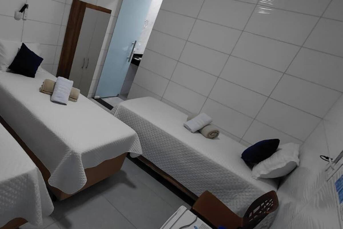 Ein Hotelzimmer mit drei Einzelbetten, jedes mit einem Kopfkissen und einem zusammengerollten Handtuch.