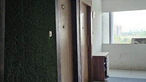 Een moderne hotellobby met een receptiebalie, twee houten deuren, een groen gestructureerde wand en een groot raam met uitzicht op de stad.