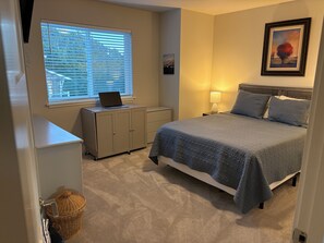 Ein Schlafzimmer mit einem Bett, einem Schreibtisch mit Laptop, einer Lampe und einem gerahmten Bild an der Wand.