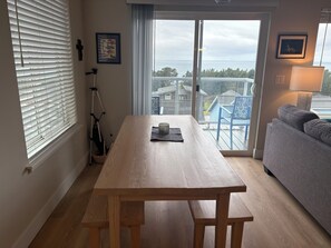 Ein Holztisch mit Bänken, ein blauer Stuhl, ein graues Sofa und Meerblick durch eine Glastür.