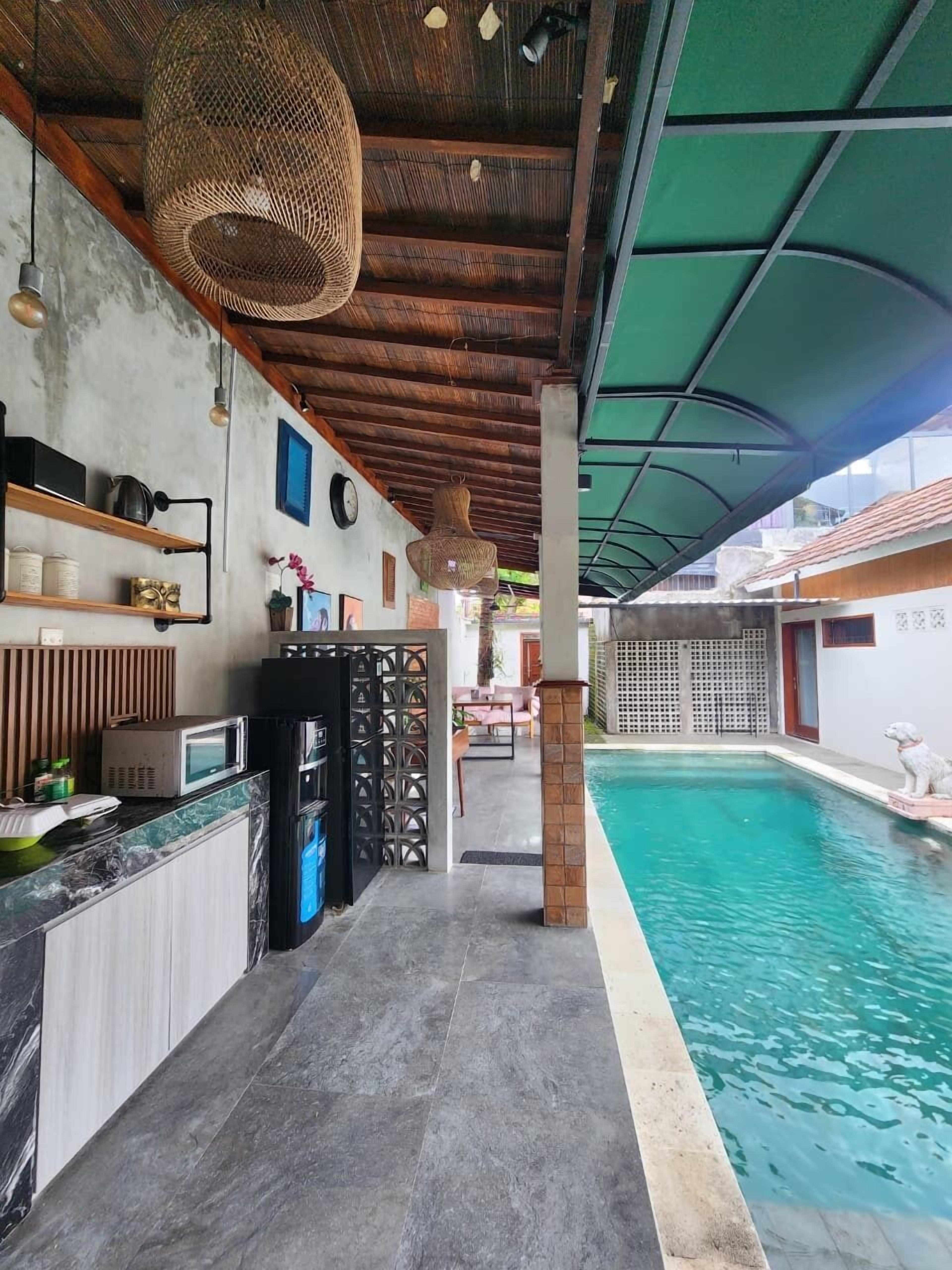 Un área junto a la piscina con un espacio de descanso cubierto, un bar con encimera de mármol y una piscina con borde de piedra.