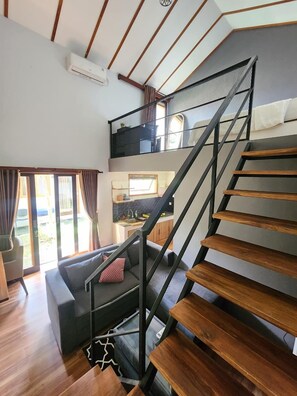 Un interior moderno con una escalera de madera, una sala de estar con un sofá y una cocina al fondo.