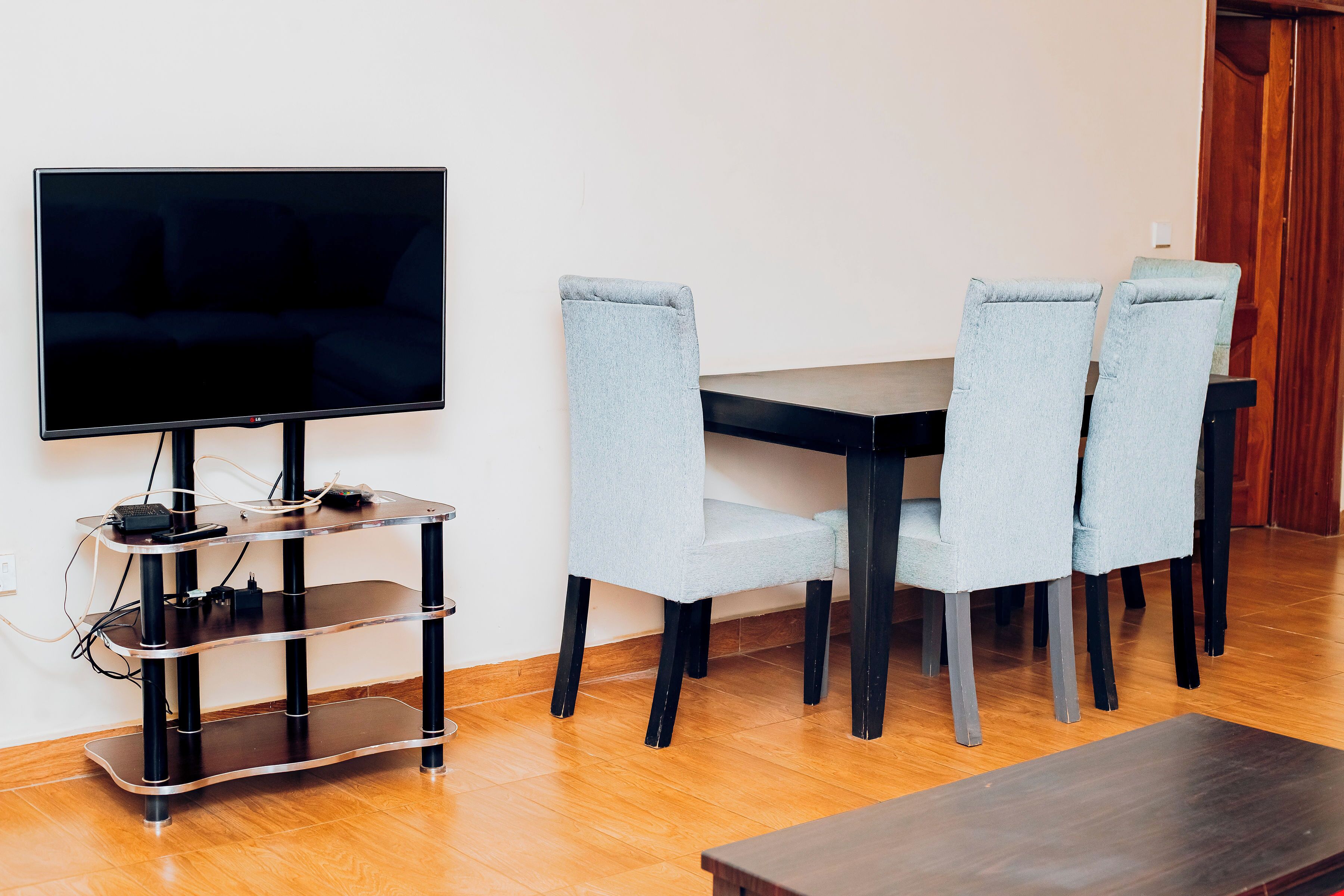 Un salon moderne avec un téléviseur à écran plat posé sur un meuble noir, une table basse en bois et quatre fauteuils bleu clair à revêtement clair, disposés autour d’une table en bois foncé.
