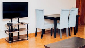 A modern living room with a flat-screen TV on a black stand, a wooden coffee table, and four light blue upholstered chairs around a dark wooden table. - Lovely 2-bedroom apartment in vibrant Kigali perfect for your stay (Kigali)