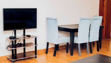 Un salon moderne avec un téléviseur à écran plat posé sur un meuble noir, une table basse en bois et quatre fauteuils bleu clair à revêtement clair, disposés autour d’une table en bois foncé.