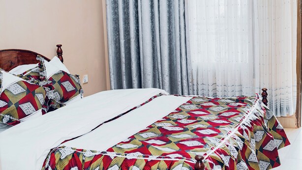 A neatly made bed with patterned bedding, a wooden headboard, and a window with sheer curtains. - Lovely 2-bedroom apartment in vibrant Kigali perfect for your stay (Kigali)