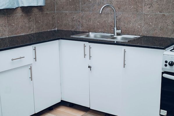 Una cocina con armarios blancos, un lavamanos de acero inoxidable y una estufa.