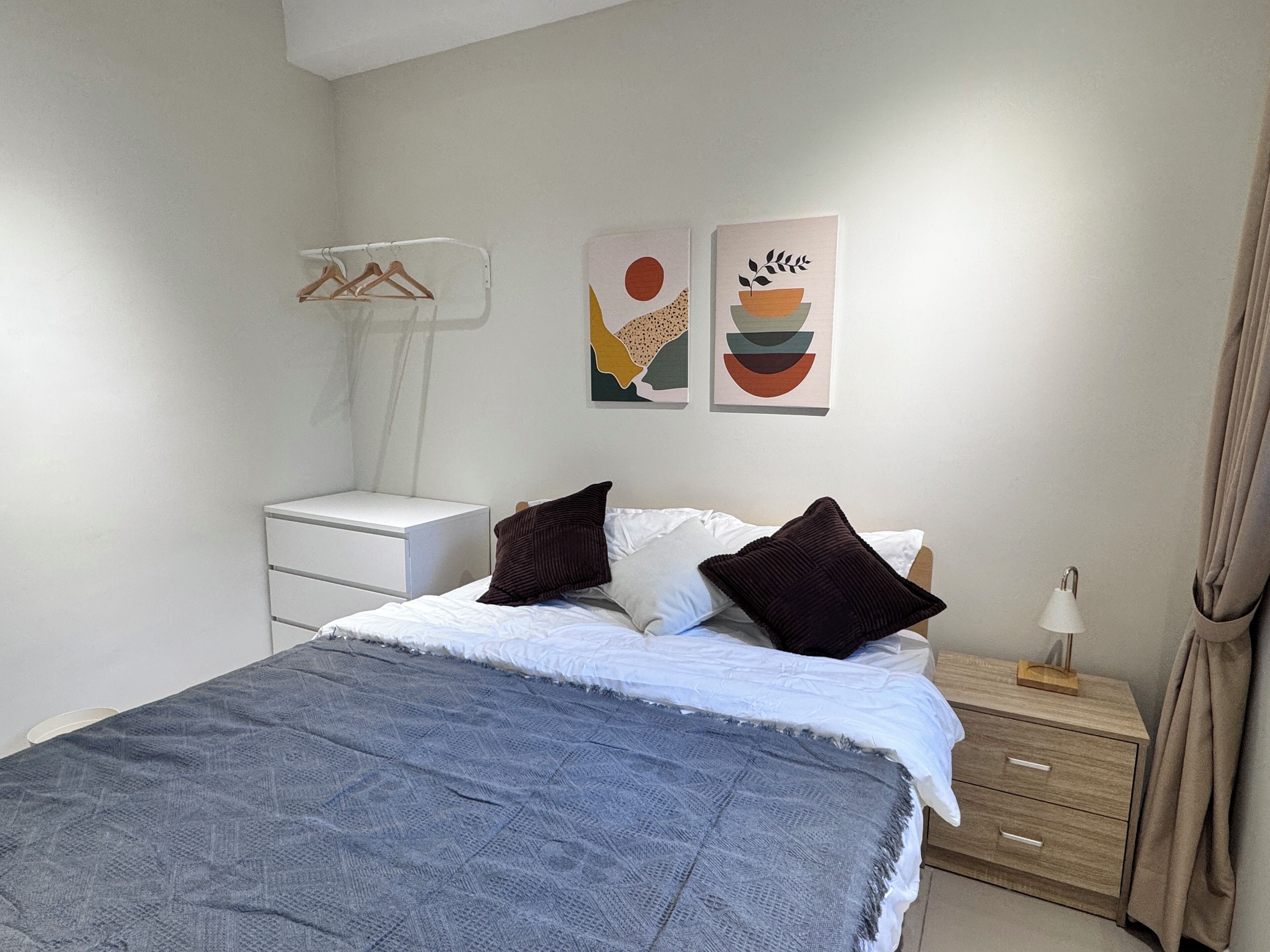 A bedroom with a bed, a nightstand, a lamp, and two wall art pieces.