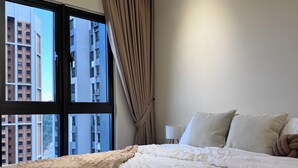 A bedroom with a large bed, a window with curtains, and a view of buildings outside. - Comfy Damansara Petaling Jaya 3BR2B  (Petaling Jaya)