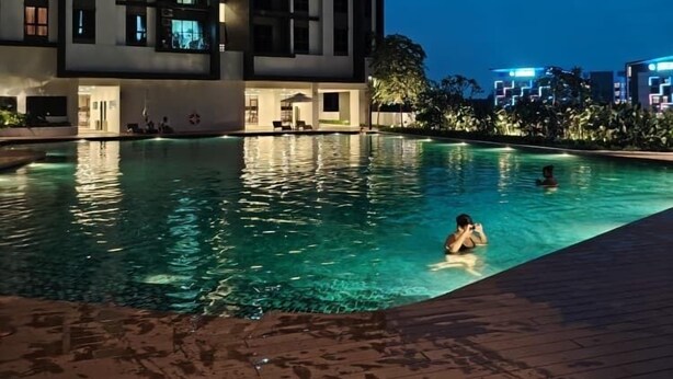 A swimming pool with people in the water, surrounded by a high-rise building with illuminated windows. - Comfy Damansara Petaling Jaya 3BR2B  (Petaling Jaya)