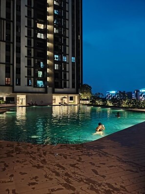 A swimming pool with people in the water, surrounded by a high-rise building with illuminated windows. - Comfy Damansara Petaling Jaya 3BR2B  (Petaling Jaya)