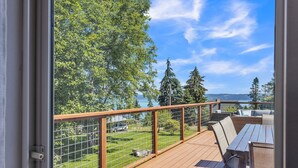 Eine Holzterrasse mit Blick auf eine Wiese und Bäume, ein Holztisch und ein Metallgeländer.