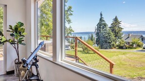 Ein Zimmer mit einem Teleskop auf einem Stativ in der Nähe eines großen Fensters mit Blick auf eine Wiese und Bäume.