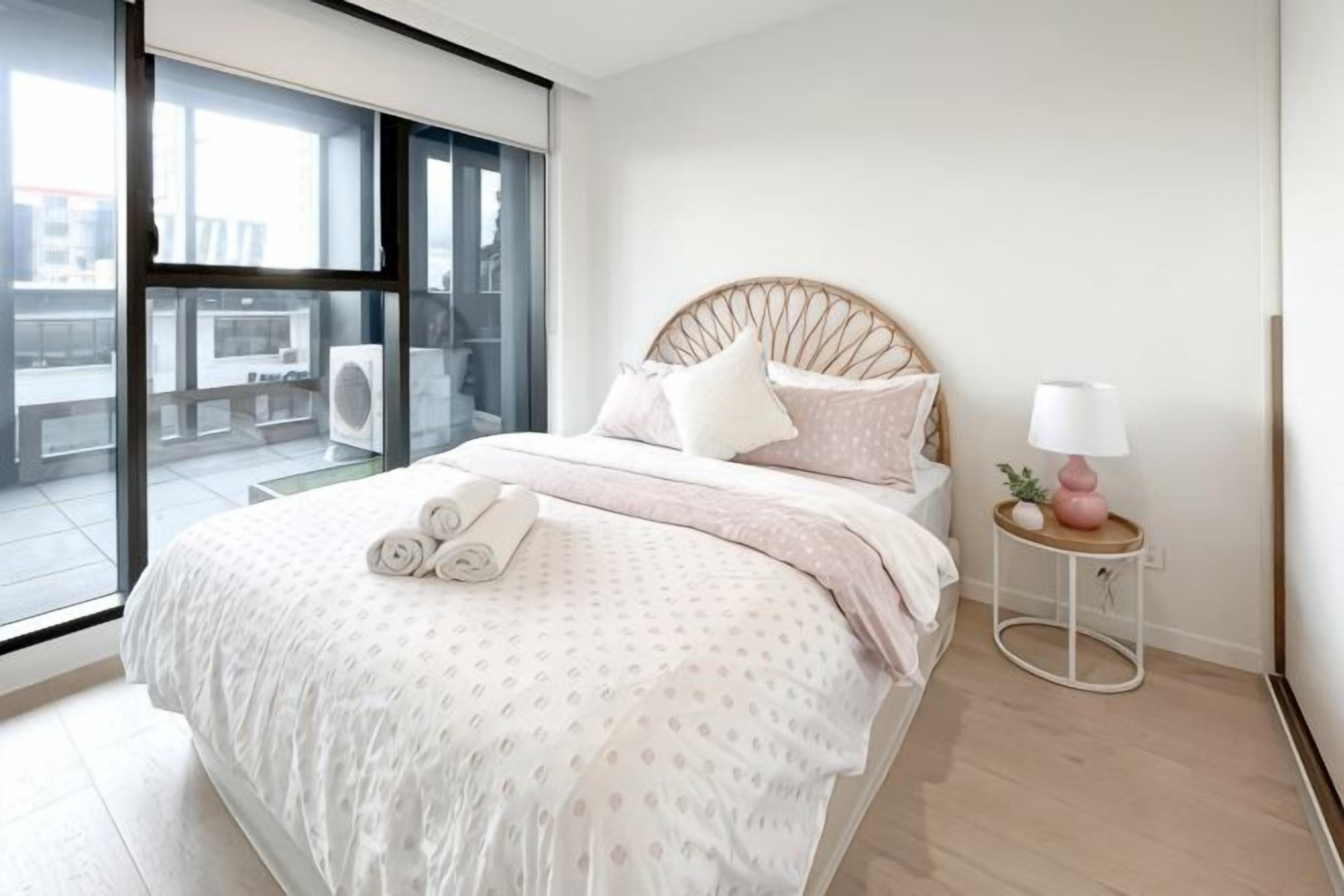 A bedroom with a bed, a bedside table with a lamp, and a view through a large window.