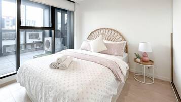 A bedroom with a bed, a bedside table with a lamp, and a view through a large window.