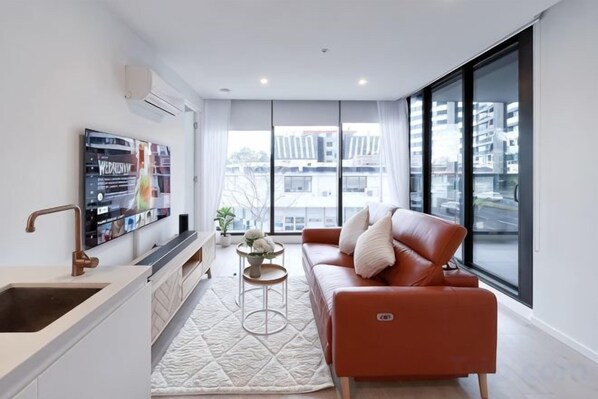 Un salon moderne avec un canapé, un téléviseur, un coin cuisine et de grandes fenêtres.