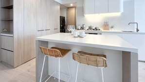 Een moderne keuken met een wit aanrecht, twee barkrukken en een inbouwoven.