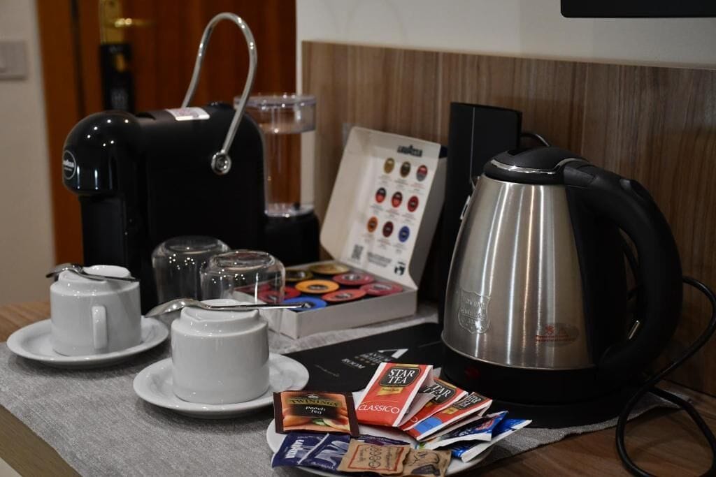 A coffee station with a coffee maker, two cups, a kettle, and a box of tea packets.