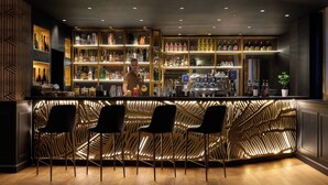 A bar area with a modern design, featuring a bar counter, three black bar stools, and a variety of bottles and glasses on shelves. - Antum Hotel (Benevento)