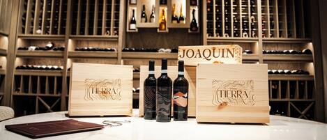 Wooden wine boxes with bottles labeled 'TIERRA' and 'JOAQUIN' in a wine cellar with shelves of wine bottles.