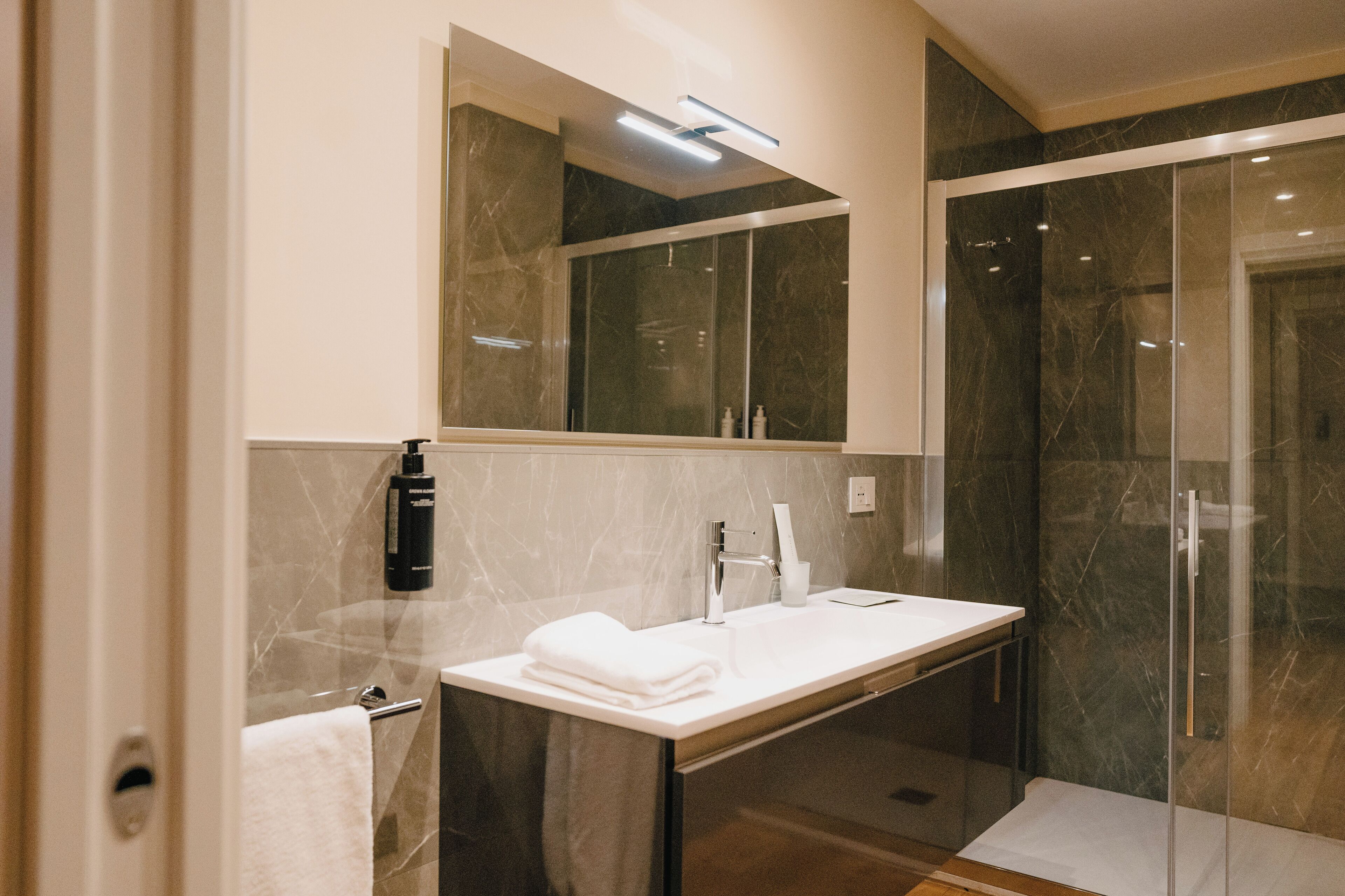 A modern bathroom with a marble vanity, a large mirror, and a glass shower enclosure.