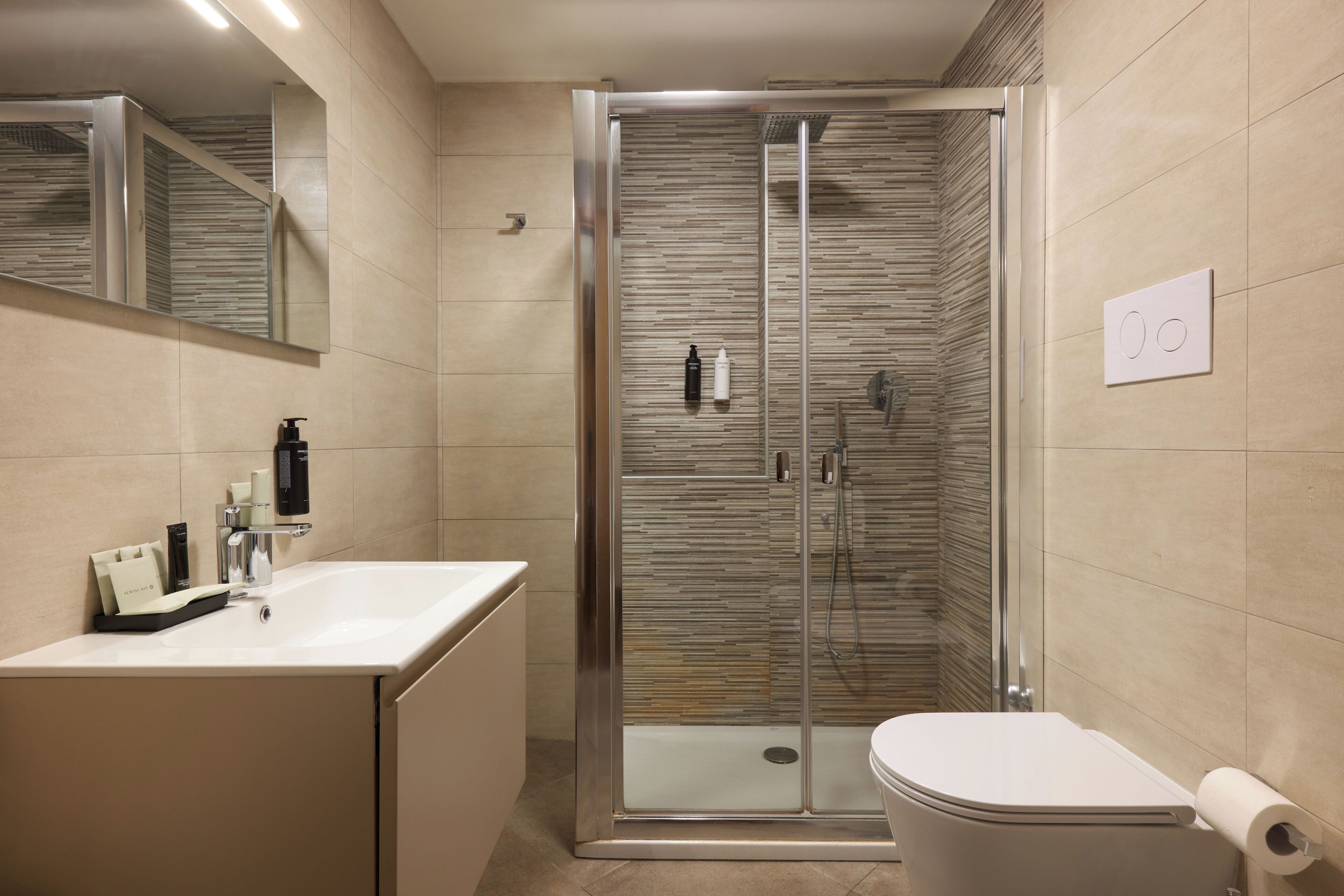 A modern bathroom with a glass-enclosed shower, a white sink with toiletries, and a toilet with a toilet paper holder.