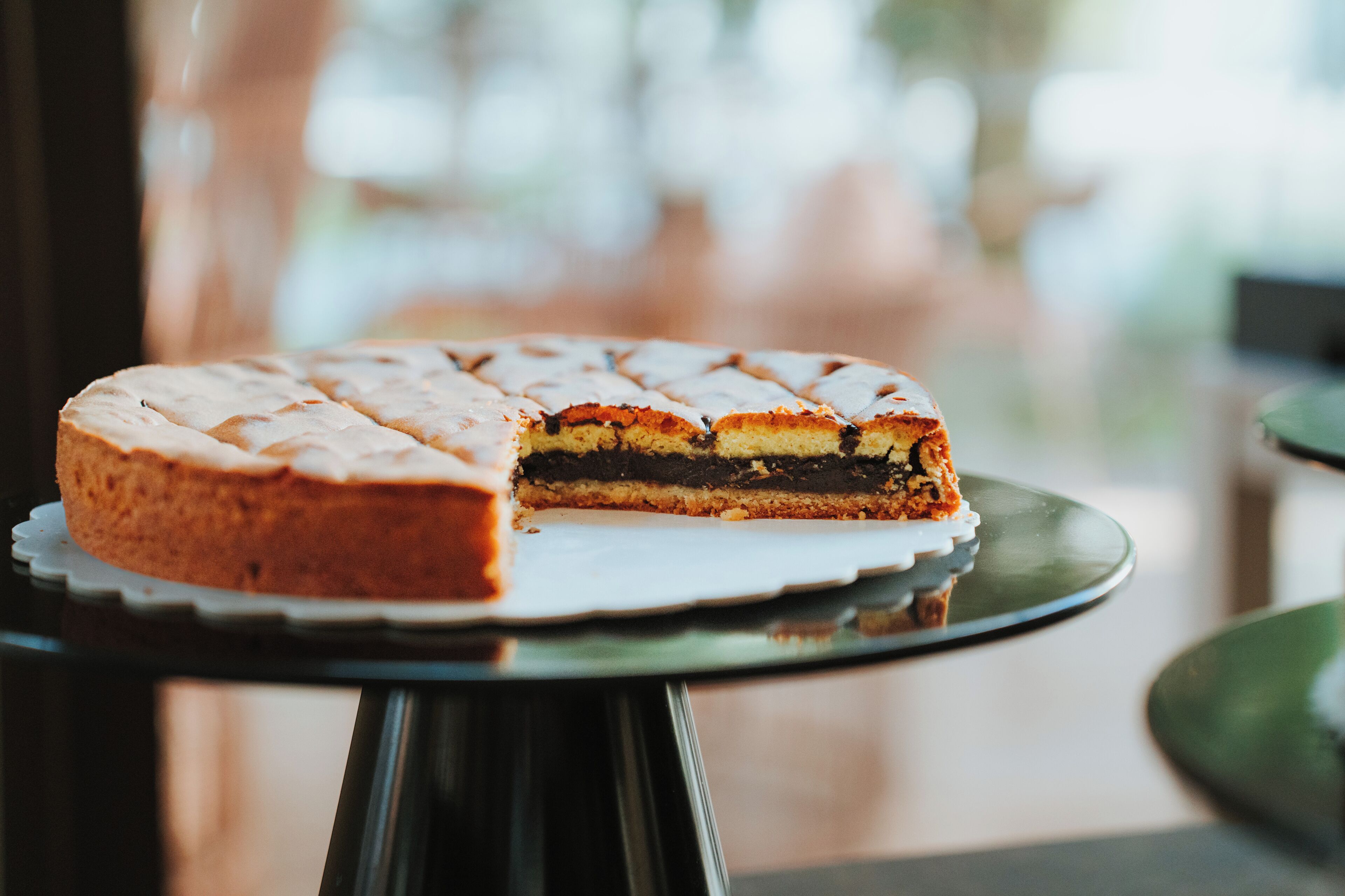 A round cake with a white frosting and a slice cut out, placed on a reflective black tray.