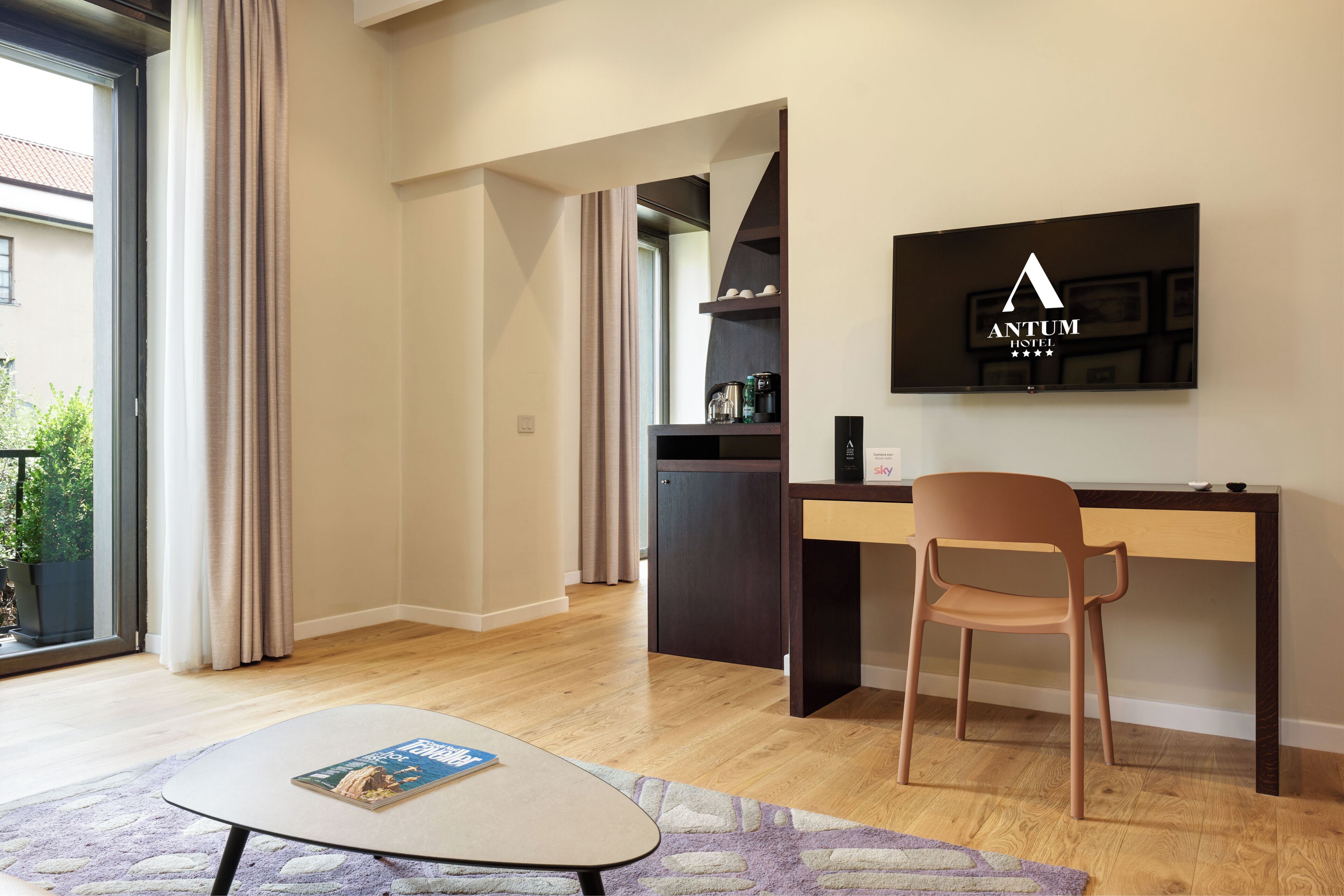 Een moderne hotelkamer met een houten bureau, een stoel, een flatscreen televisie en een tijdschrift op een bijzettafeltje.