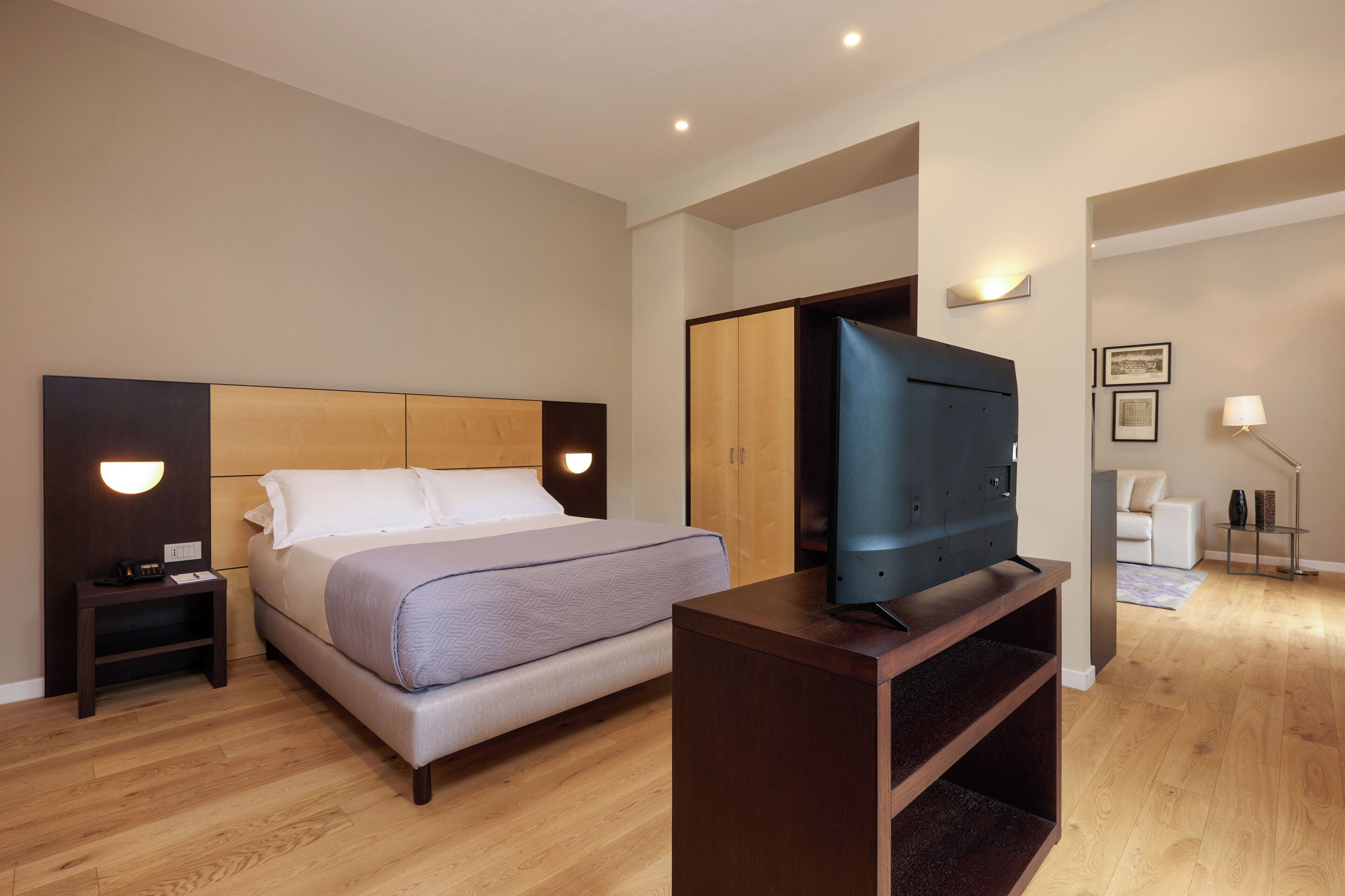 A hotel room with a bed, a desk, a television, a chair, and a lamp.