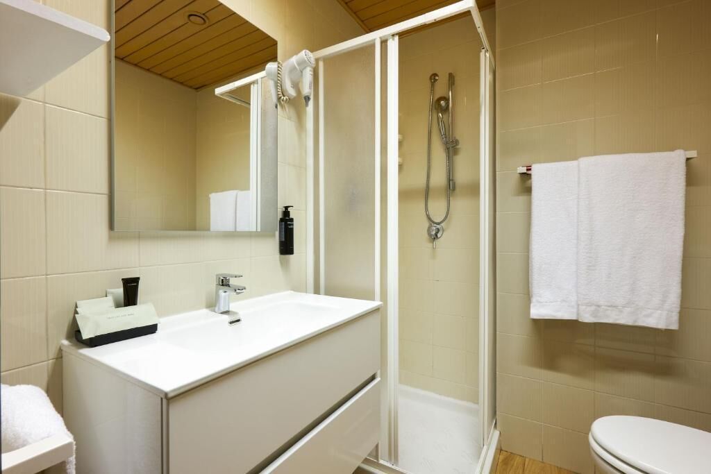 Un baño con lavamanos blanco, espejo, cabina de ducha e inodoro.
