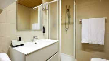 Un baño con lavamanos blanco, espejo, cabina de ducha e inodoro.