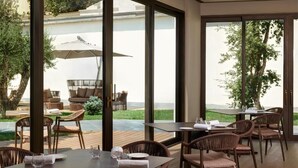 An outdoor dining area with wicker furniture and large windows overlooking a garden. - Antum Hotel (Benevento)