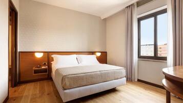 A hotel room with a bed, bedside table, and a window with curtains.