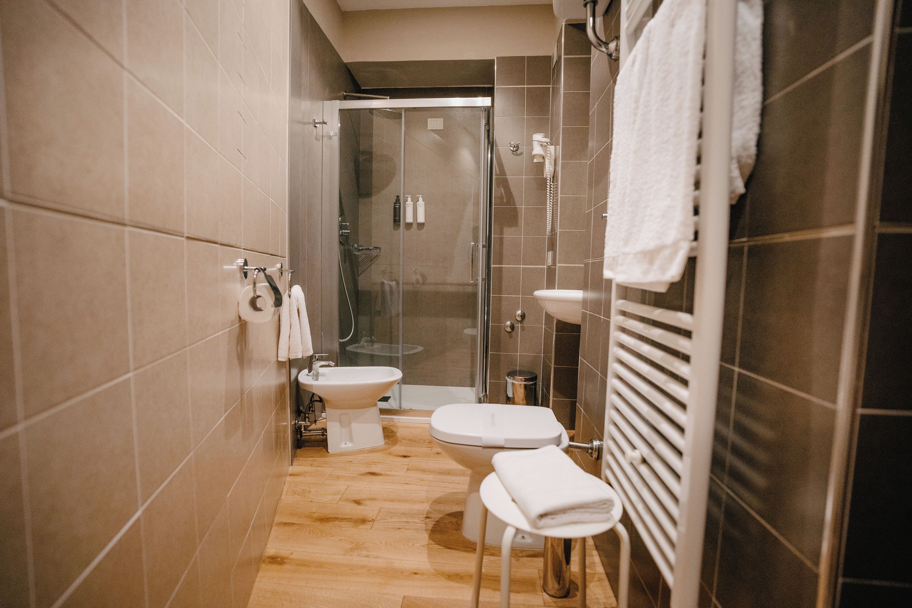 A modern bathroom with a shower, toilet, bidet, and a small stool.