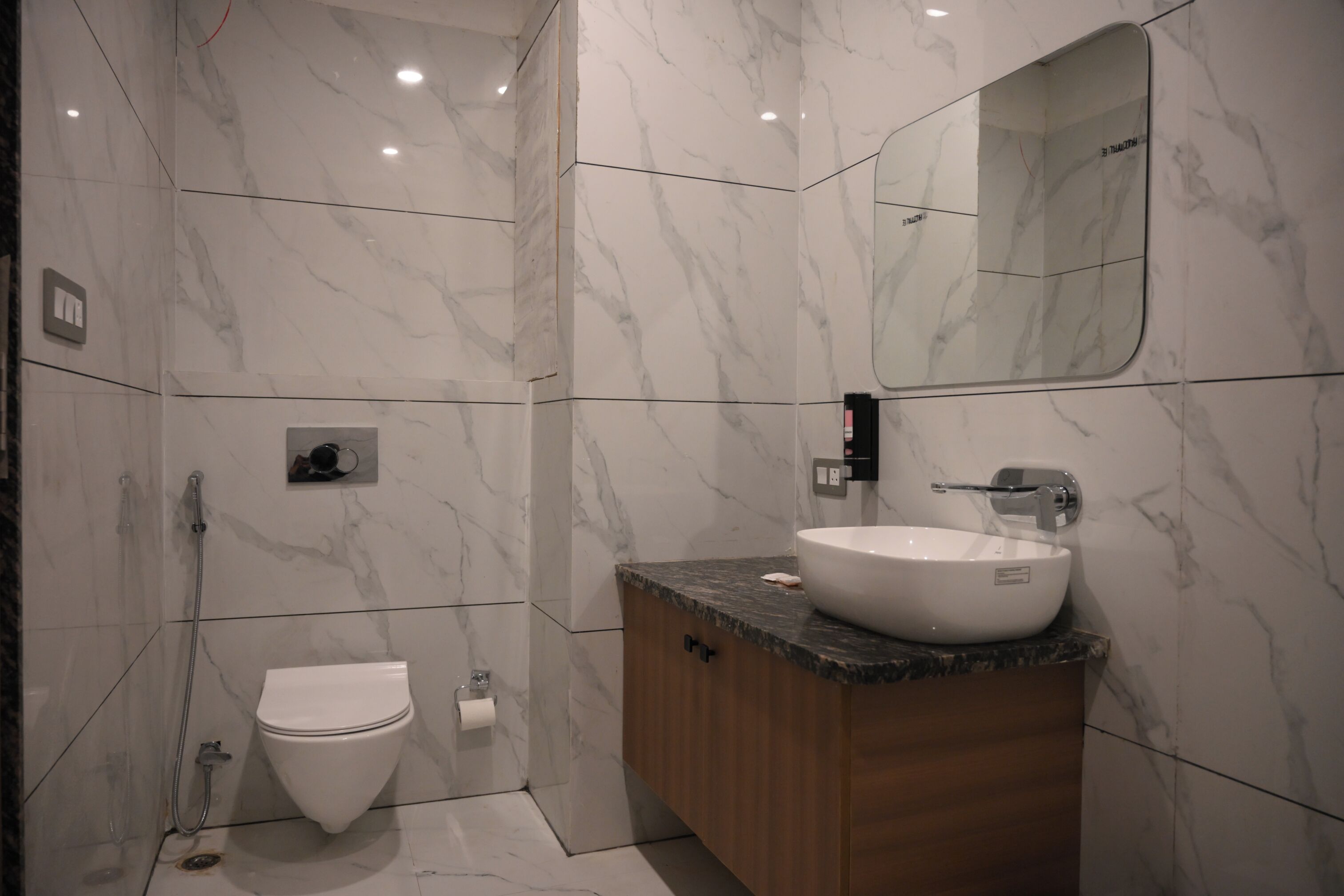 A modern bathroom with a marble floor, a white toilet, a wooden vanity with a sink, and a mirror.