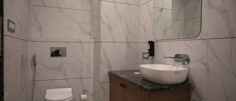 A modern bathroom with a marble floor, a white toilet, a wooden vanity with a sink, and a mirror.