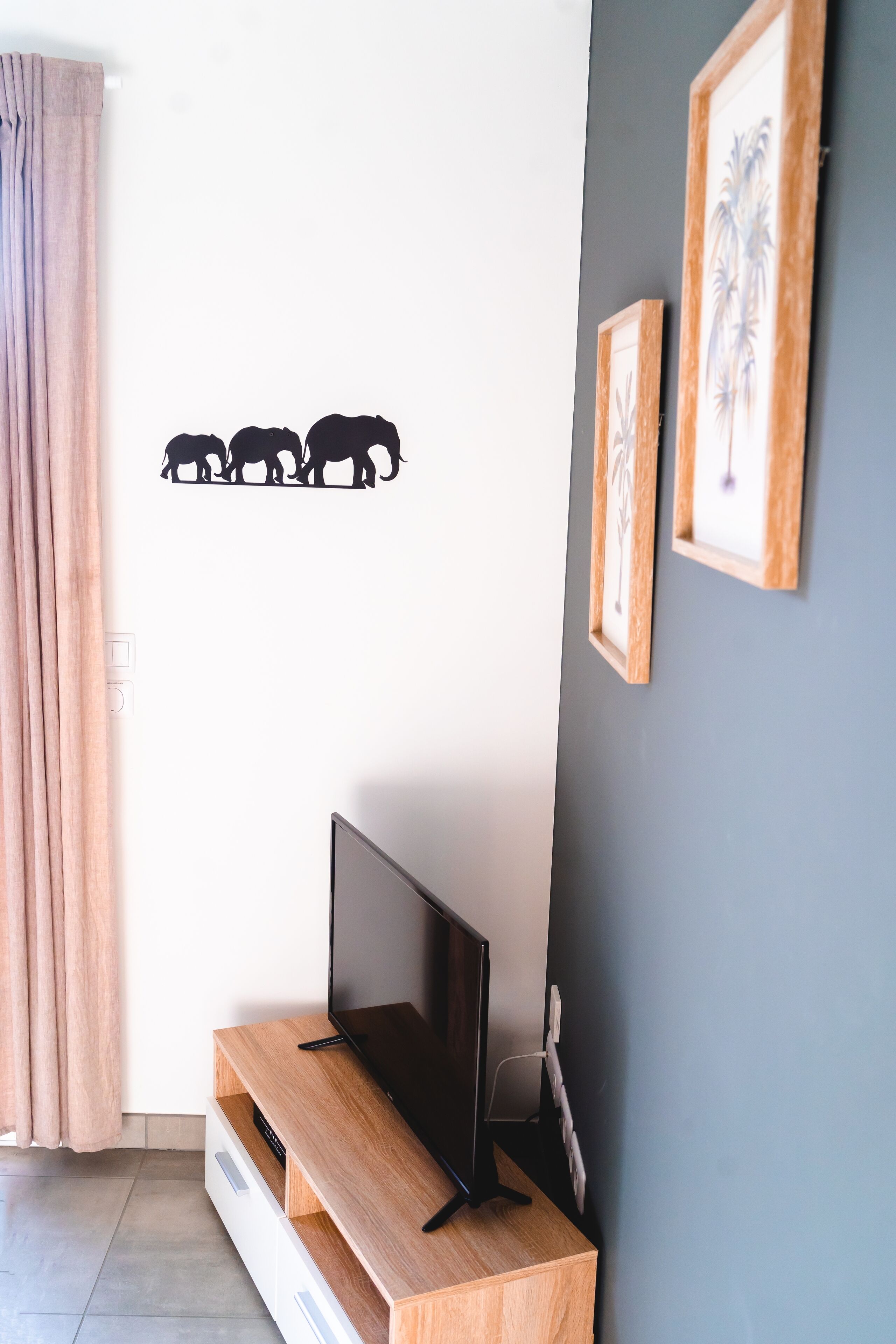 A room with a TV on a wooden stand, a wall with a bear decal, and two framed pictures.